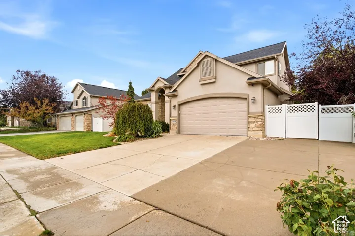 Two-story exterior featuring a neutral stucco facade, stone veneer accents, an attached three-car garage, and white vinyl privacy fencing