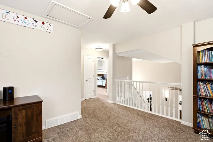 Open interior landing featuring wall-to-wall carpeting, white wooden baluster railings, a ceiling fan with integrated lighting, and neutral wall tones