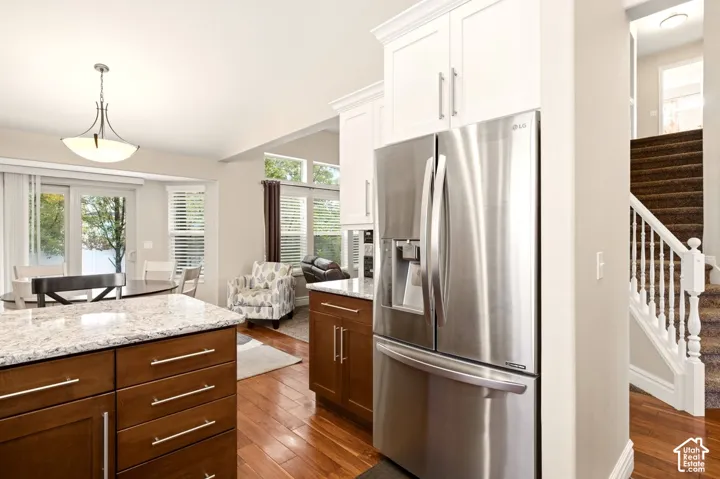 Kitchen featuring wood-finish flooring, two-tone cabinetry with upper white and lower wood-finish units, stone countertops, stainless steel refrigerator, and recessed lighting