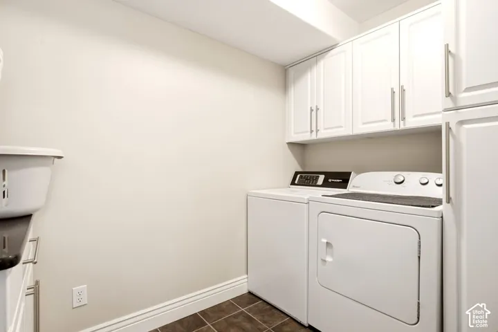 Utility area featuring white shaker-style cabinetry, dark tile flooring, and a dedicated storage pantry
