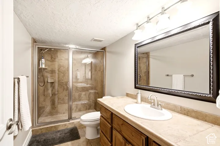 Bathroom featuring a walk-in shower with tile surround, wood cabinetry, stone-finish countertop with an integrated basin, and a wall-mounted framed mirror