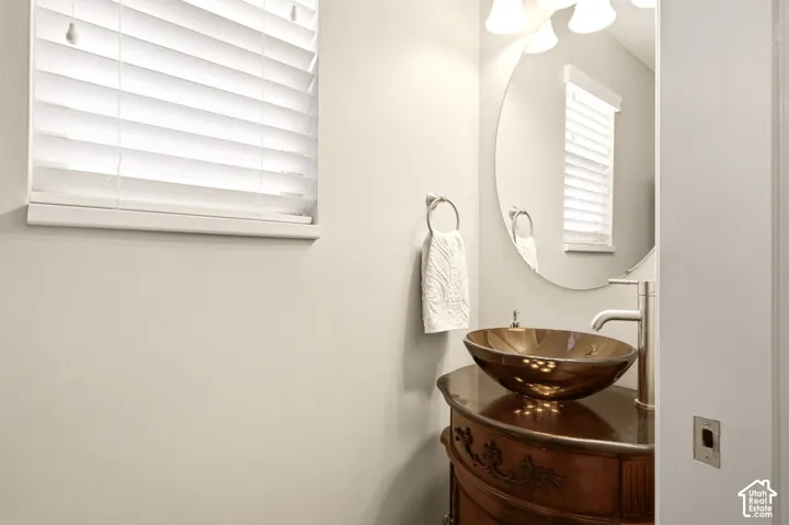 Oval vanity cabinet with ornate carved detailing, topped by a rounded glass vessel sink and a tall brushed-metal faucet, accompanied by a frameless oval mirror and polished multi-bulb light fixture