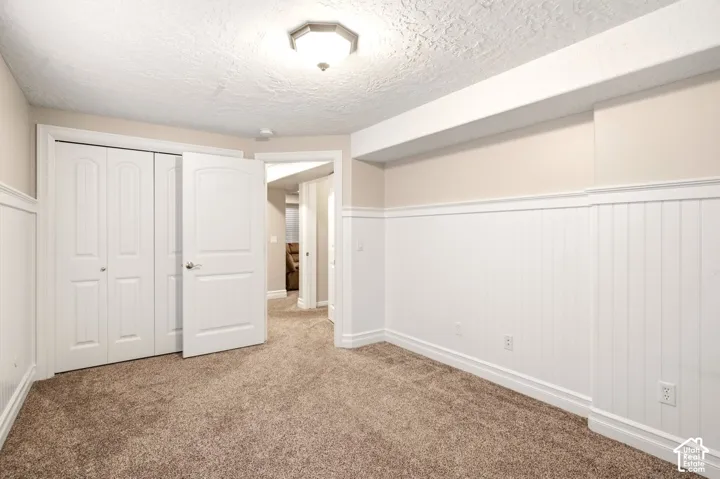 Room featuring white beadboard wainscoting, carpeted flooring, a closet with folding panel doors, and a flush-mount light fixture