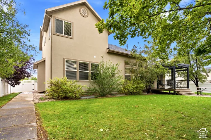 Stucco exterior siding, elevated deck with a pergola, concrete side walkway, white vinyl privacy fencing, and mature landscaping