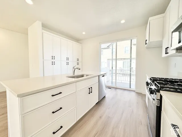 Kitchen featuring white shaker-style cabinetry, matte black hardware, quartz countertops, wood-finish flooring, and a stainless steel undermount sink