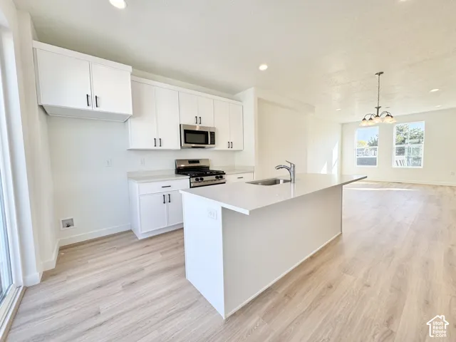 Kitchen featuring white shaker-style cabinetry, quartz countertops, a central island with an undermount sink, recessed lighting, and wood-finish flooring