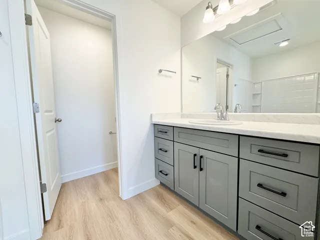 Bathroom featuring gray shaker-style cabinetry, a stone-finish countertop with an integrated basin, wood-finish flooring, a large wall-mounted mirror, and matte black hardware