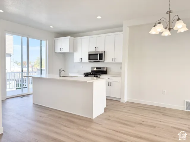 Kitchen featuring white cabinetry, quartz countertops, a central island with a stainless steel faucet, wood-finish flooring, and a multi-light chandelier