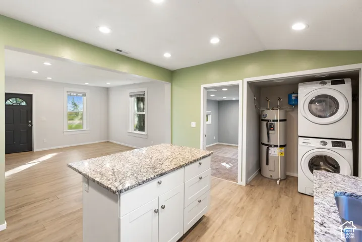 Kitchen featuring a central island with stone-finish countertop, white shaker-style cabinetry, recessed ceiling lighting, and wood-finish flooring