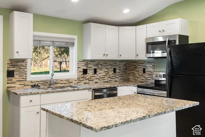 Kitchen featuring white shaker-style cabinetry, patterned stone-finish countertops, multicolored mosaic tile backsplash, stainless steel appliances, and recessed lighting