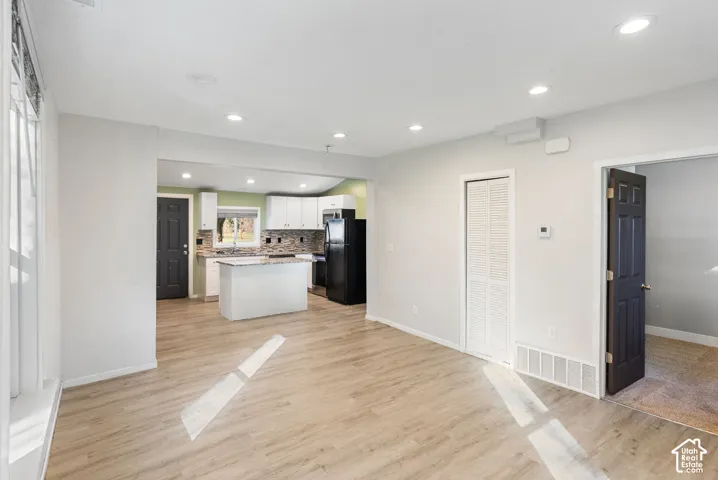 Open-concept interior featuring wood-finish flooring, recessed lighting, white shaker-style cabinetry, and a central kitchen island