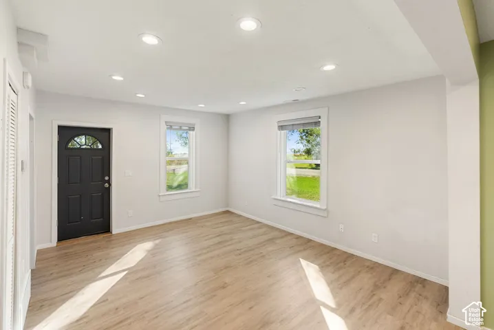 Interior space featuring wood-finish flooring, recessed lighting, neutral wall paint, dual windows, and a dark-toned exterior door with a semi-circle glass panel