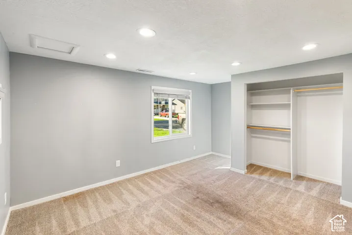 Neutral-toned interior featuring recessed lighting, plush carpeting, a single-pane window, and a built-in closet with integrated shelving and hanging rods