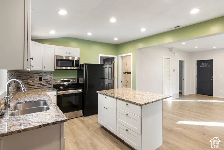 Kitchen featuring a central island, stone-finish countertops, tile backsplash, white shaker-style cabinetry, and wood-finish flooring