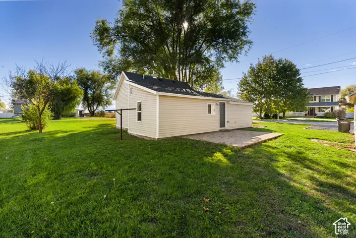 Expansive backyard featuring a large grass lawn, mature trees, and a paved patio area