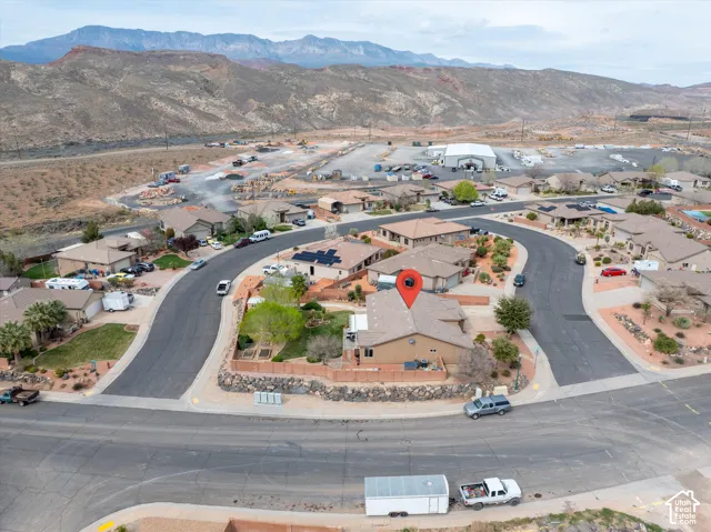 Aerial perspective of a property featuring solar panels, a tiered rock retaining wall, and mountain backdrops