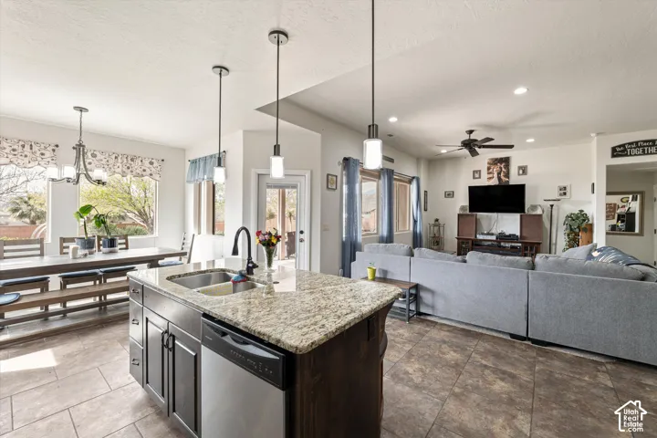 Kitchen featuring an island with a stone-finish countertop, dual-basin stainless steel sink, dark wood-finish cabinetry, and stainless steel dishwasher