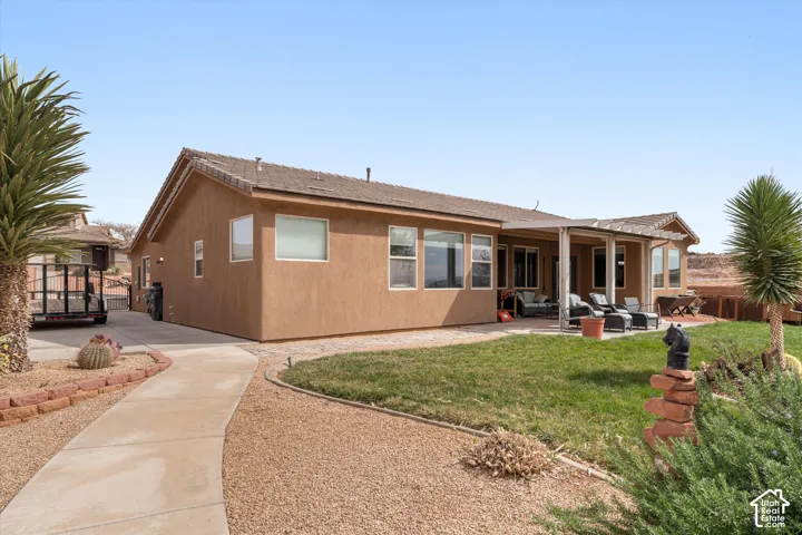 Stucco exterior featuring a covered patio, concrete walkway, manicured lawn, and desert-inspired landscaping