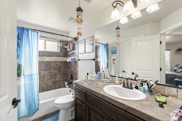 Bathroom featuring dark wood-finish cabinetry, tile-surround bathtub with decorative inlay, tile countertop, undermount oval sink, and a full-width vanity mirror with integrated lighting