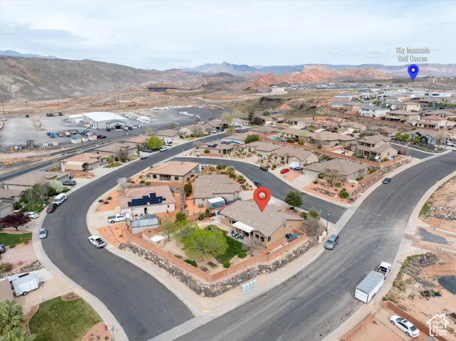 Aerial perspective of a single-story residence on a corner lot featuring a walled perimeter, rear patio, solar panel array, and established landscaping