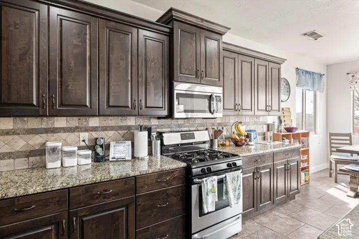 Kitchen featuring dark-stained cabinetry, stone-finish countertops, stainless steel appliances, and a decorative tile backsplash