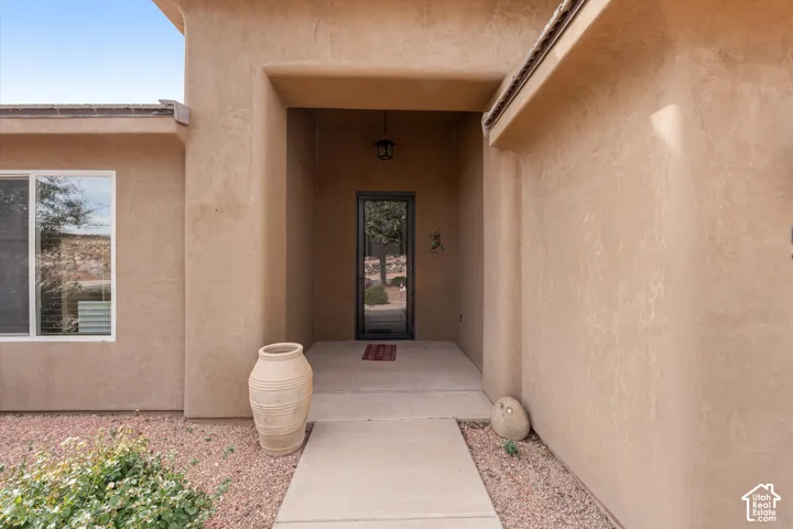 Stucco exterior entryway featuring a concrete walkway, recessed porch, single-light glass front door, and overhead pendant fixture