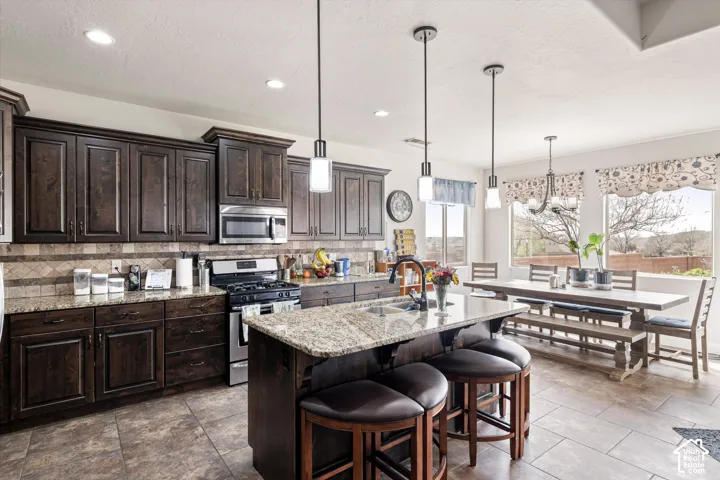 Kitchen featuring custom dark-wood cabinetry, stone-finish countertops, tile flooring, an expansive central island, and stainless steel appliances
