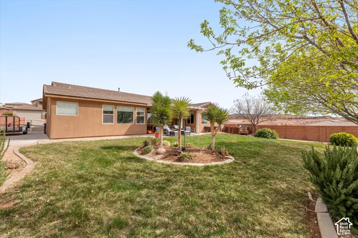 Rear exterior featuring a stucco facade, covered patio, manicured lawn, established landscaping, and perimeter masonry wall