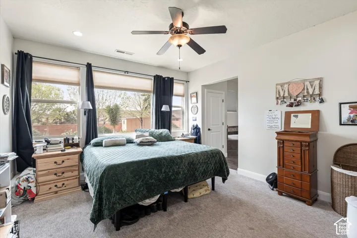Neutral-toned room featuring plush wall-to-wall carpeting, large windows with natural light, and a ceiling fan with integrated lighting