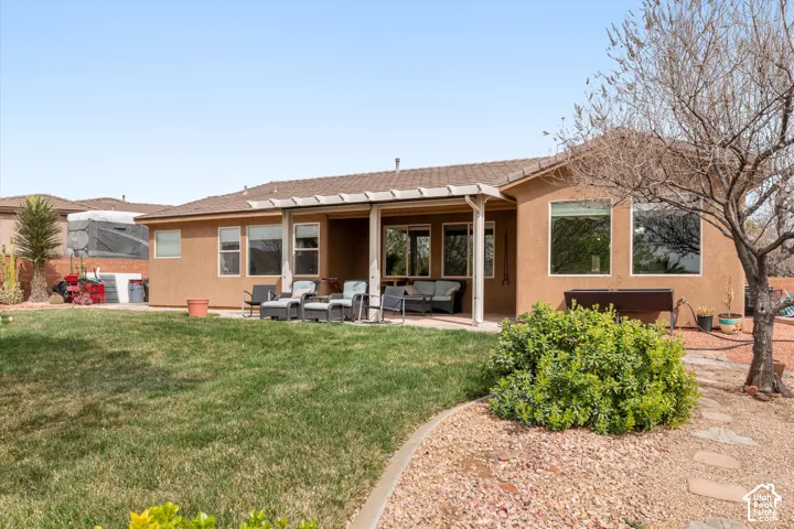 Stucco exterior with a covered rear patio, metal pergola, mature landscaping, and gravel ground cover