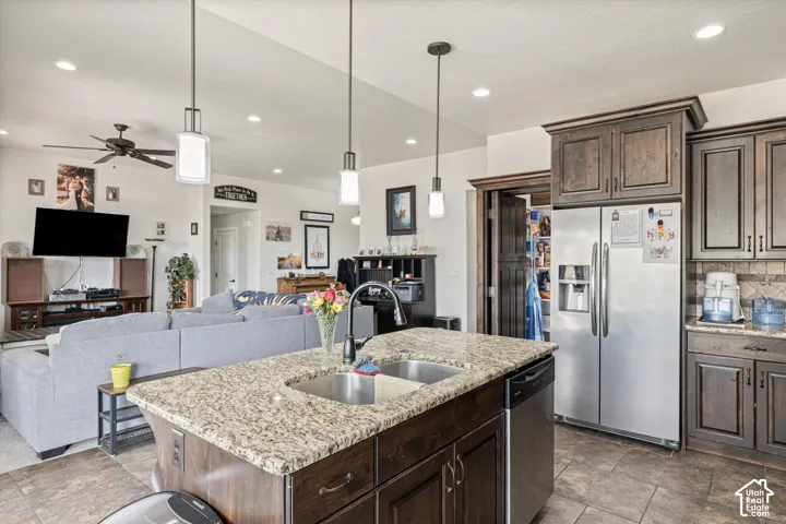Kitchen featuring dark wood cabinetry, stone countertops, a central island with a double-basin sink, stainless steel appliances, and recessed lighting