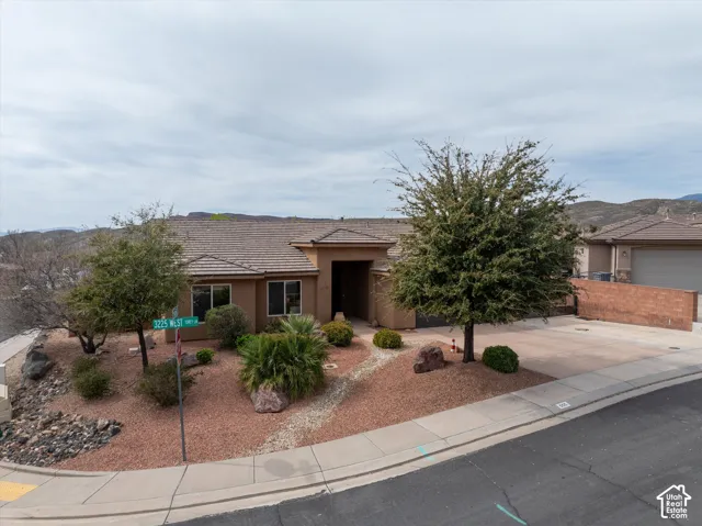 Stucco exterior featuring a tile roof, concrete driveway, and xeriscaped front yard with mature trees and decorative rock