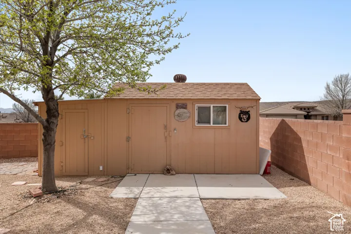 Outbuilding featuring tan composite siding, a shingled roof, a horizontal sliding window, and concrete pad entryway, enclosed by a masonry block wall