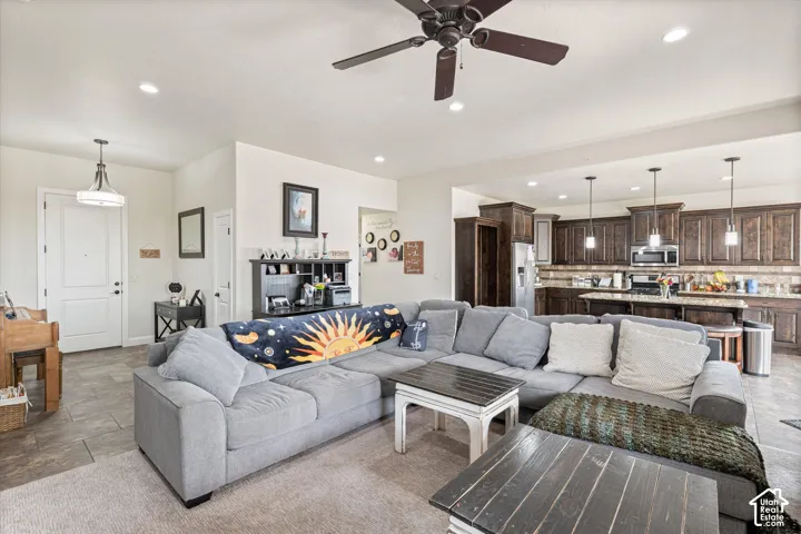 Open-concept interior featuring dark-stained cabinetry, a large kitchen island with pendant lighting, stone-finish countertops, tile flooring, and a ceiling fan