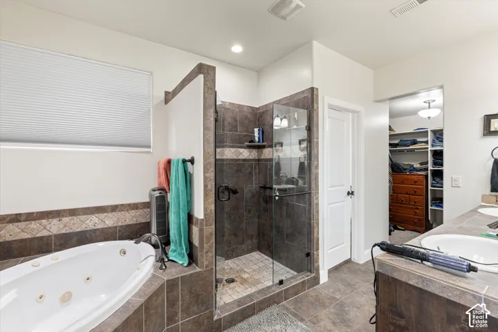 Jetted soaking tub and walk-in shower with tiled surround, dual-sink vanity with tile countertop, and built-in closet shelving