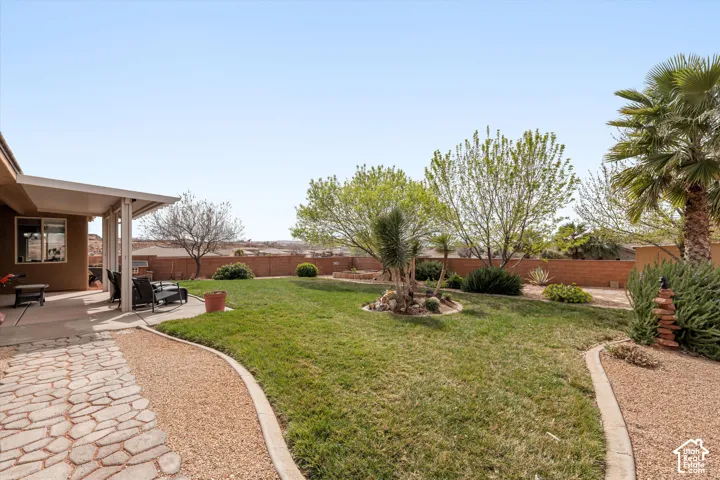 Backyard featuring a concrete patio, stone paver walkway, manicured lawn, and mature trees enclosed by a masonry wall