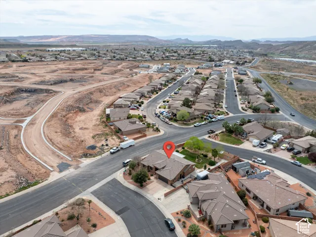 Aerial view of residential property featuring a corner lot location, concrete driveway, attached multi-car garage, and desert landscape surroundings