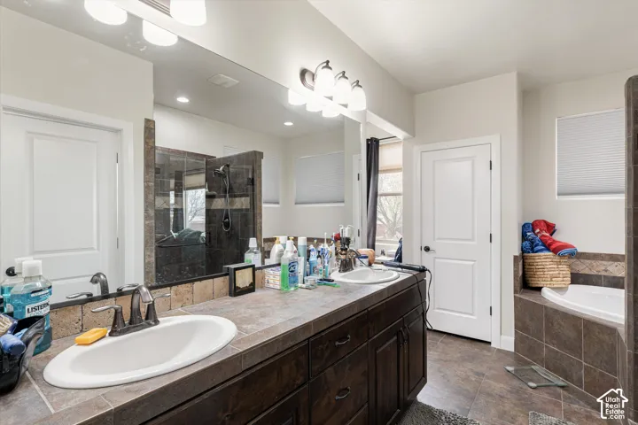 Dual-sink vanity with tile countertop, dark wood cabinetry, large vanity mirror, and built-in soaking tub with tile surround