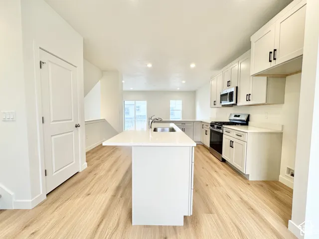 Kitchen featuring white shaker-style cabinetry, an expansive center island with a stainless steel sink, stone-surface countertops, wood-finish flooring, and recessed lighting
