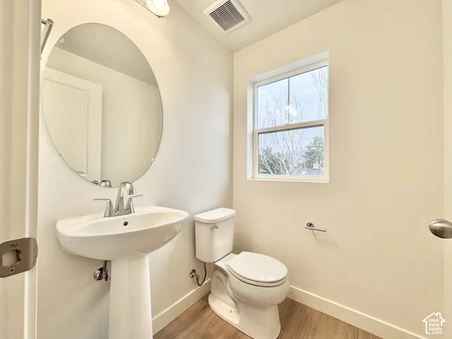 Pedestal sink featuring a polished chrome faucet, large oval wall-mounted mirror, single-hung window, and wood-finish flooring