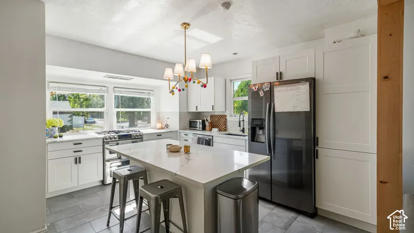 Kitchen featuring white shaker-style cabinetry, a central island with a solid surface countertop, slate-toned tile flooring, and a multi-arm chandelier
