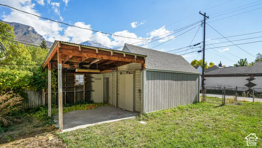 Detached storage structure featuring a covered carport, wood-frame construction, corrugated metal roofing, and vertical siding, set against a mountain backdrop