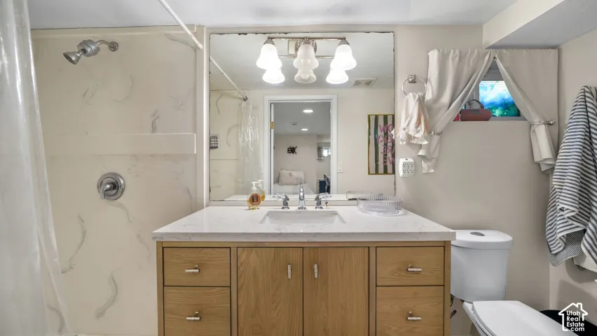 Bathroom vanity featuring a stone-composite countertop, undermount sink, and light-toned wood cabinetry, complemented by a large wall-mounted mirror and a three-light fixture