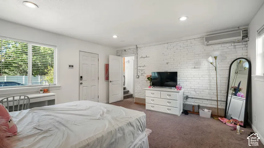 Interior space featuring white-painted exposed brick wall, recessed ceiling lighting, wall-mounted ductless air conditioning unit, and built-in window-side cabinetry