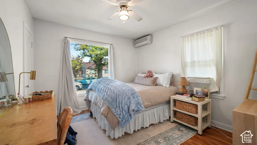 Room featuring wood-finish flooring, a ceiling fan with integrated lighting, and a wall-mounted climate control unit