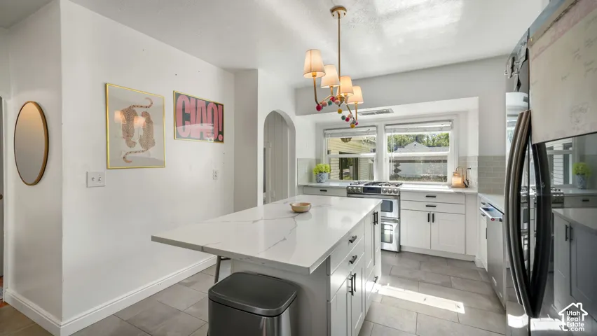 Kitchen featuring a central island with a quartz countertop, white cabinetry with matte black hardware, stainless steel appliances, and large-format tile flooring