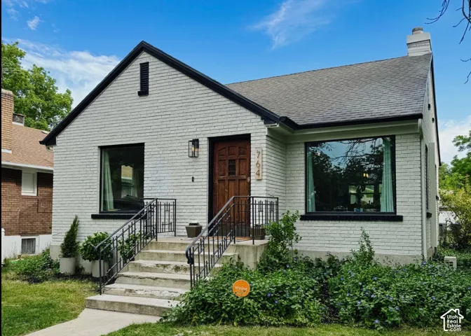 Exterior featuring painted brick facade, dark metal trim accents, arched wood front door, concrete porch stairs with custom metal railings, and large pane windows