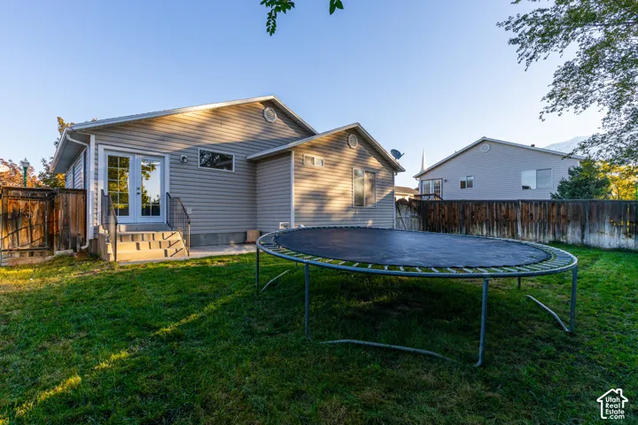 Rear exterior featuring light-colored horizontal siding, glass-paneled double doors, concrete step entry, and a wood privacy fence