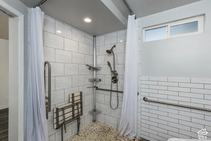 Walk-in shower featuring white rectangular wall tile, pebble-texture flooring, a hand-held showerhead, integrated seating, and metal grab bars
