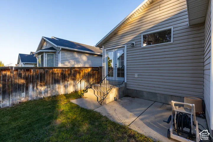 Horizontal siding exterior featuring a concrete patio, wood privacy fencing, glass-paneled double doors, and metal stair railing